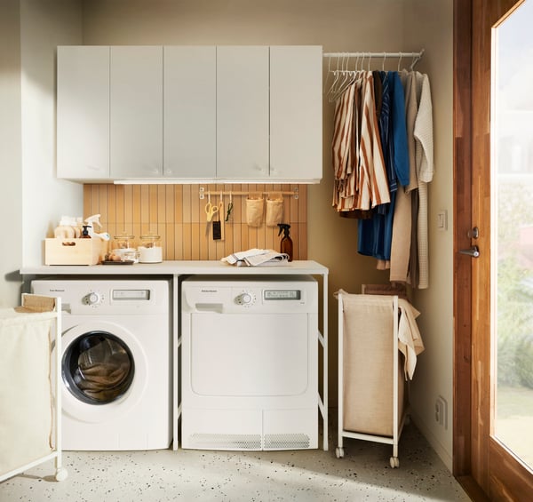 Wasruimte met witte kastjes, droger en wasmachine en twee wasmanden op wieltjes die in de ruimte staan.