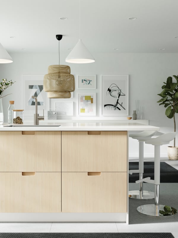 A kitchen island with a worktop in marble effect and drawer fronts in bamboo, two white bar stools and pendant lamps.