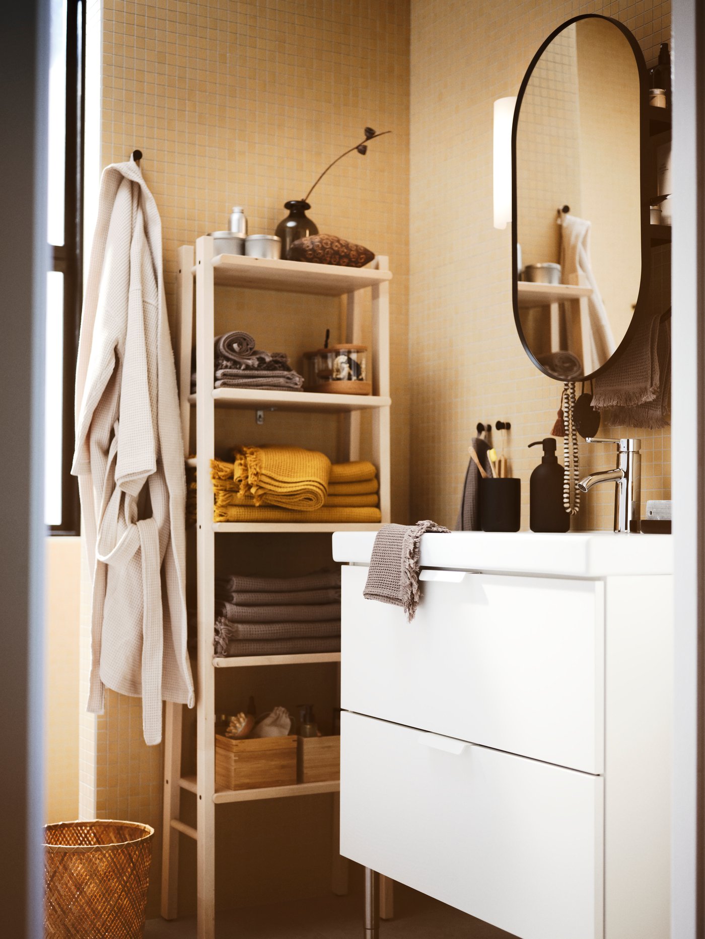 Salle de bain aux tons beiges avec meuble-lavabo GODMORGON blanc. Étagère contre le mur avec serviettes pliées. Robe suspendue au bord