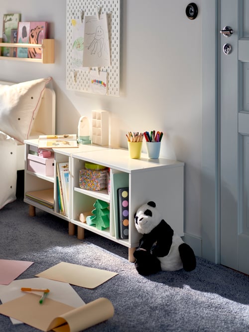 A white SMUSSLA bedside table and shelf unit displays arts, crafts and toys in a children’s bedroom.