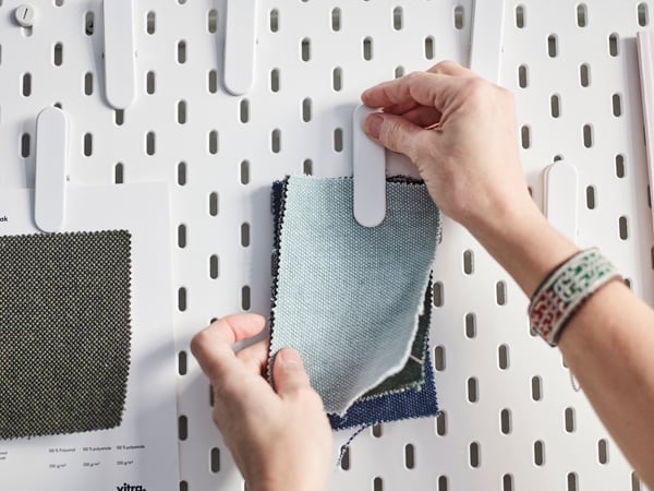 Moodboard with a hand pinning some fabrics in the wall.