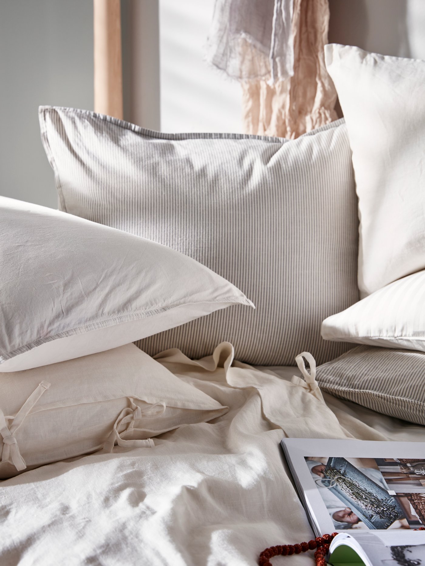 A lot of different kinds of pillows sit on a bed. An open book of colourful cartoons lies on the bed near the pillows.