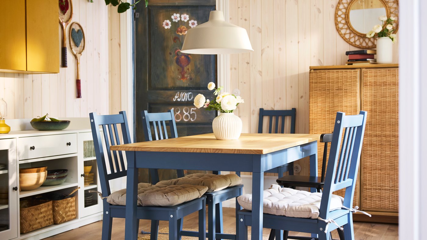 A SJÖMARKT pendant lamp hangs over a PINNTORP table and some blue stained/pine PINNTORP chairs with VIPPÄRT chair pads.