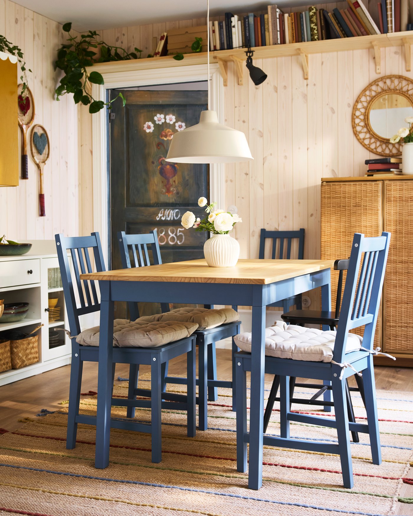 A SJÖMARKT pendant lamp hangs over a PINNTORP table and some blue stained/pine PINNTORP chairs with VIPPÄRT chair pads.
