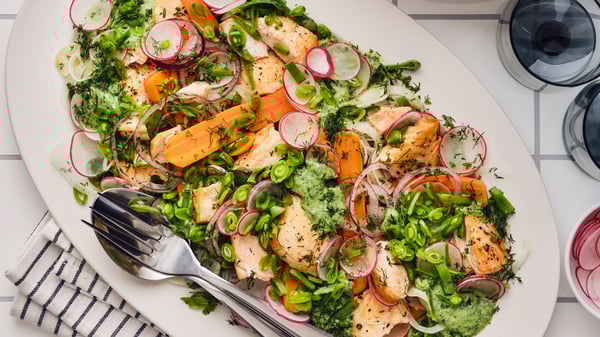 A colourful salad with grilled salmon, radishes, carrots, snap peas, and fresh herbs, served on a white plate.