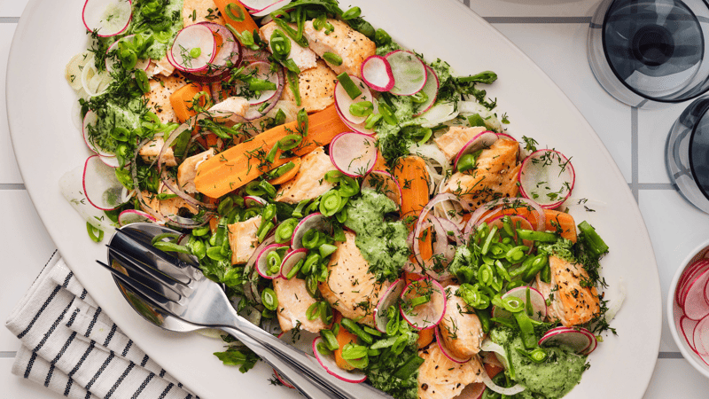 Una coloratissima insalata con salmone grigliato, ravanelli, carote, taccole ed erbe aromatiche fresche servita su un piatto bianco.