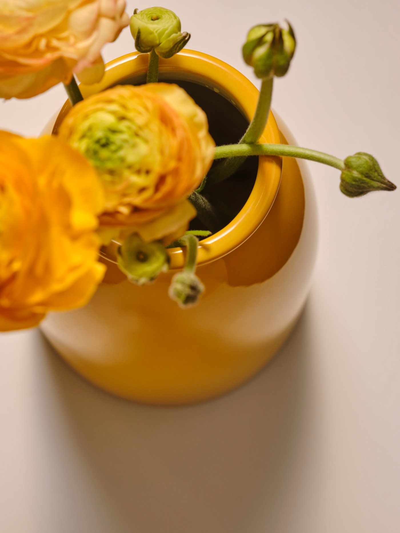 A yellow KOPPARBJÖRK vase holding multiple yellow flowers while being placed on a beige surface.