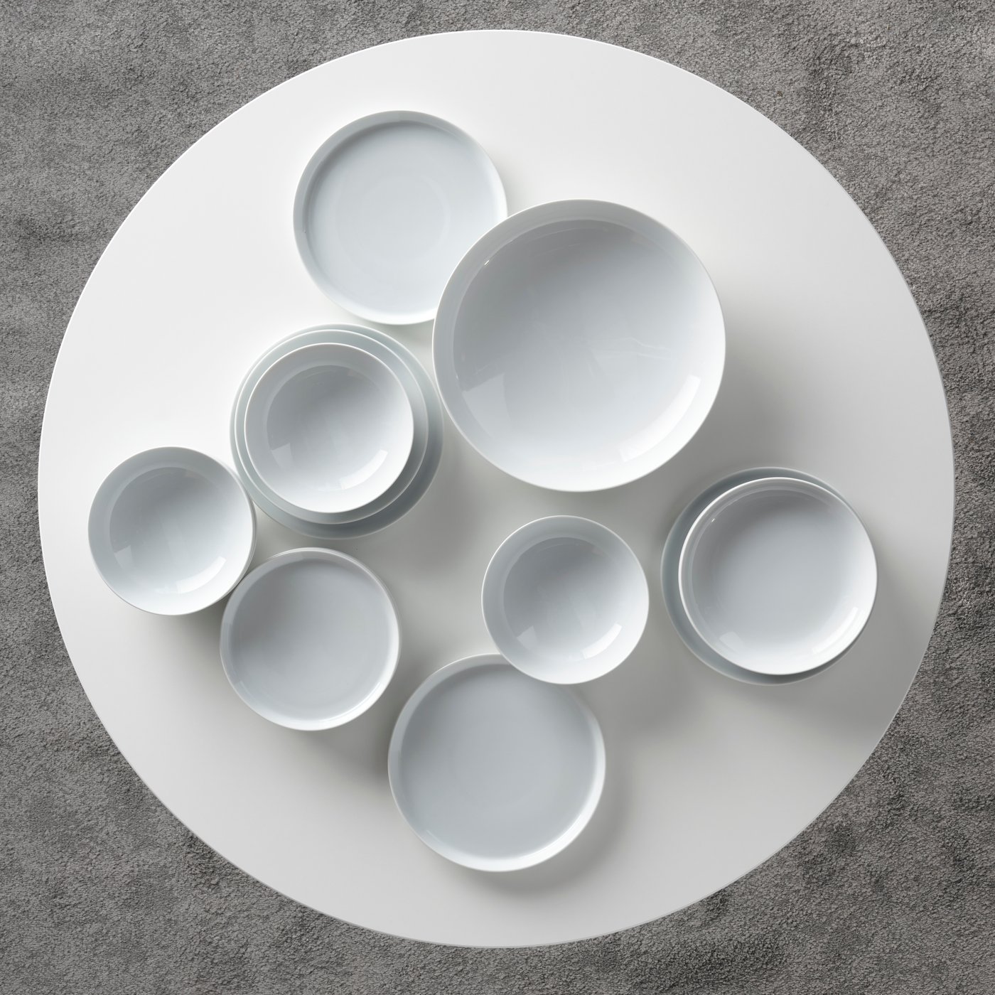 Various pieces of white crockery from the IKEA 365+ series stand on top of a round white DOCKSTA table.