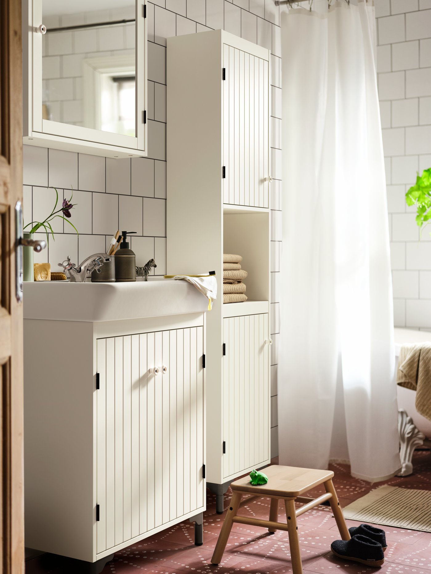 A white-tiled bathroom with a SILVERÅN cabinet surrounded by other SILVERÅN storage. Beneath stands a VILTO step stool.