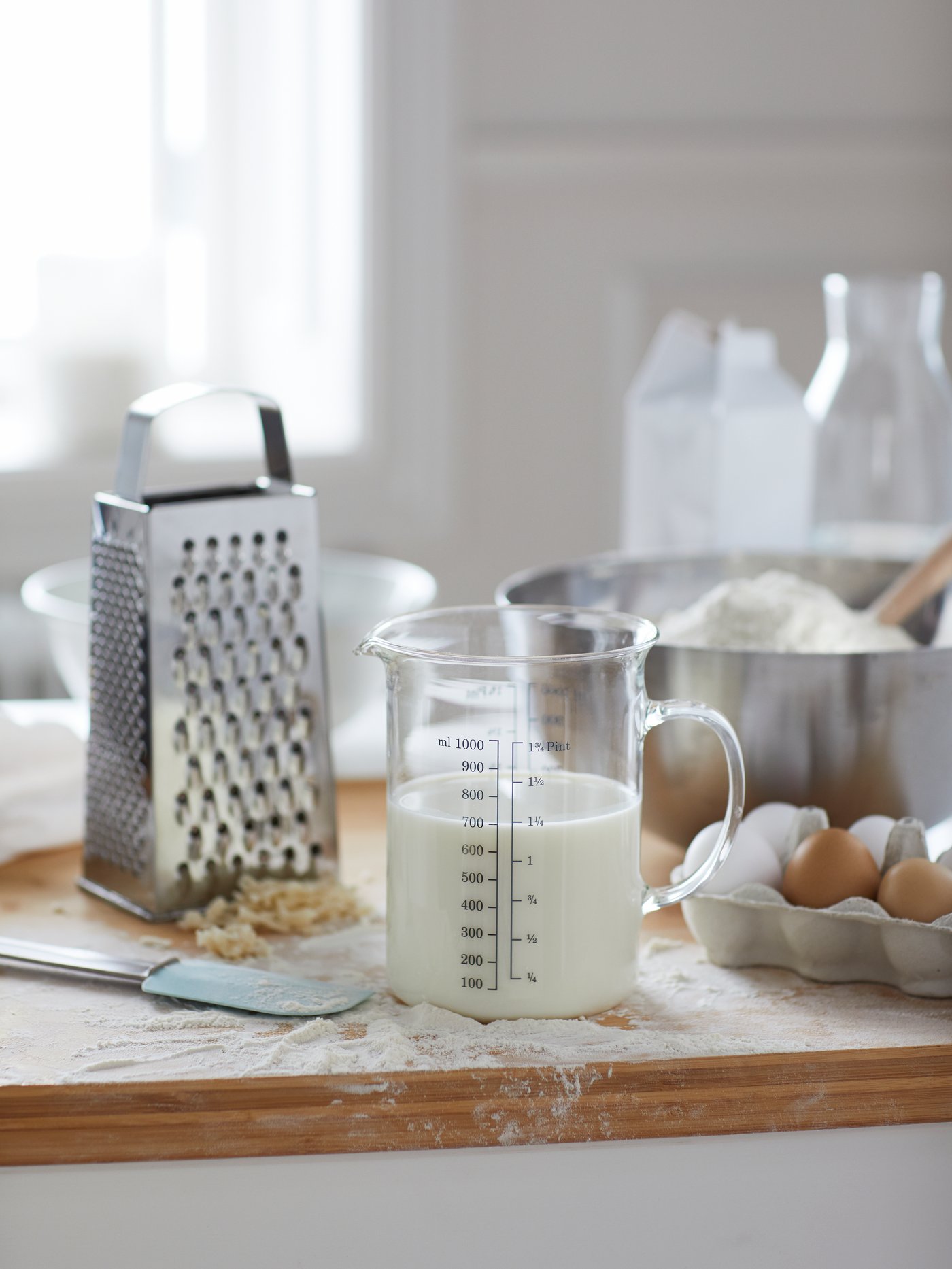 Una encimera llena de ingredientes y utensilios para preparar un postre. Hay ingredientes dentro de un bol BLANDA BLANK, leche en una jarra graduada y harina por todas partes.