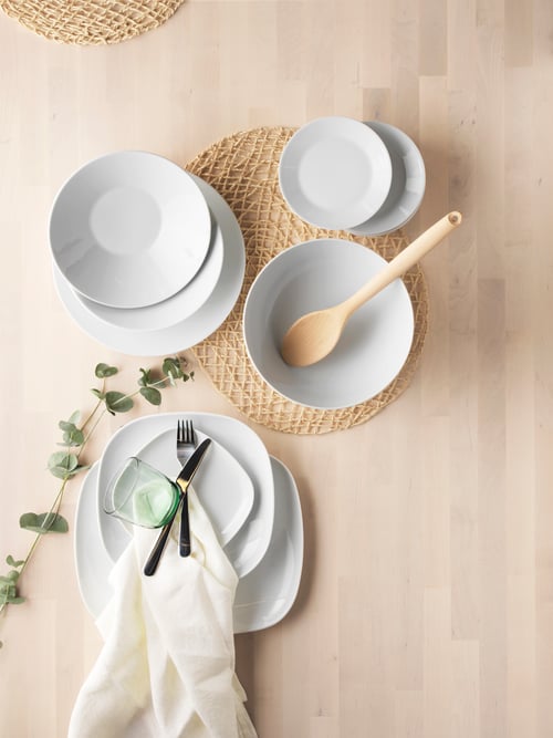 Widok z góry na nakrycie stołu z ułożonymi w stos okrągłymi talerzami z białej porcelany, beżową drewnianą łyżką, beżową podkładką pod talerze i dekoracjami.