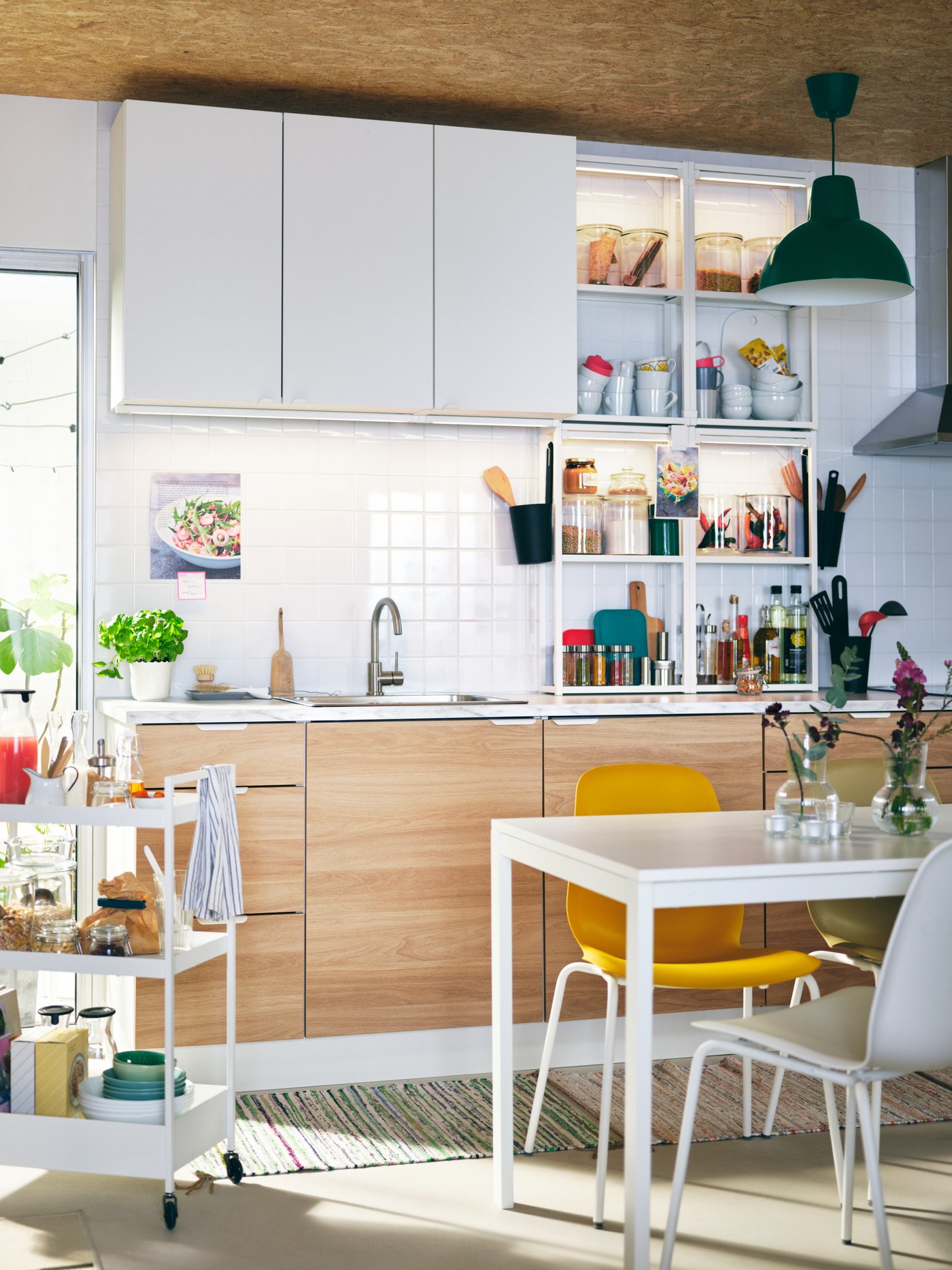 A light kitchen with ENHET cabinets, a white MELLTORP table, different-colour LEIFARNE chairs, and a white NISSAFORS trolley.