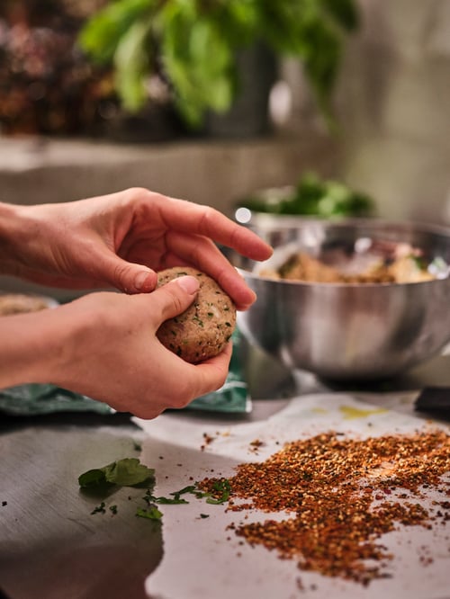A pair of hands shaping a patty of VÄRLDSKLOK plant mince by a worktop on which stands a BLANDA BLANK stainless-steel bowl.