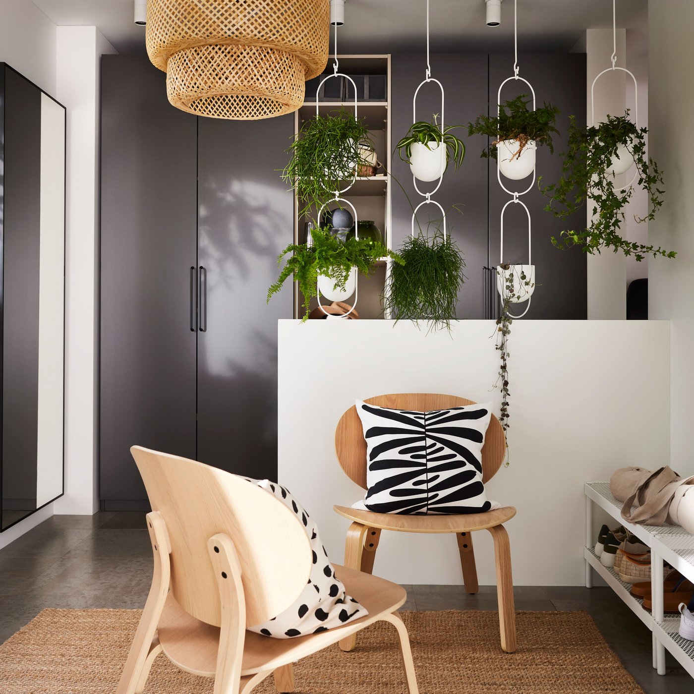 En hall med mörkgrå PAX garderober, SINNERLIG bambulampa och STÄLL skoskåp under en fönsterbräda med växter.