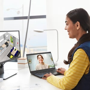 An IKEA co-worker in a blue and yellow shirt talks to a person on their laptop while reviewing a kitchen design on their monitor.