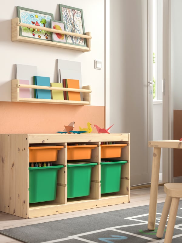 Ein TROFAST KInderzimmerregal, Kiefer weiß gebeizt, mit Boxen in hell hellorange/leuchtend grün.