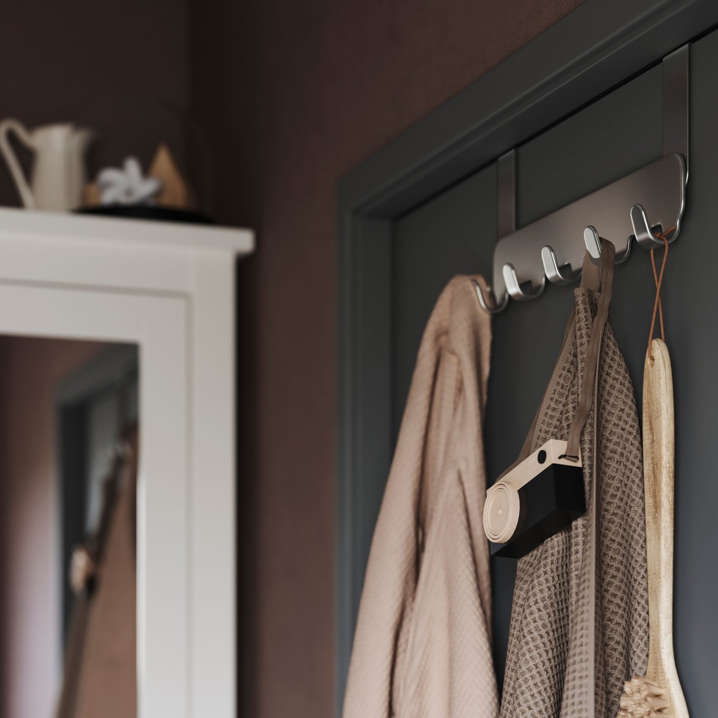 A BROGRUND hanger for door, with a towel, a bath robe and other things hanging from it, hangs on a bathroom door.