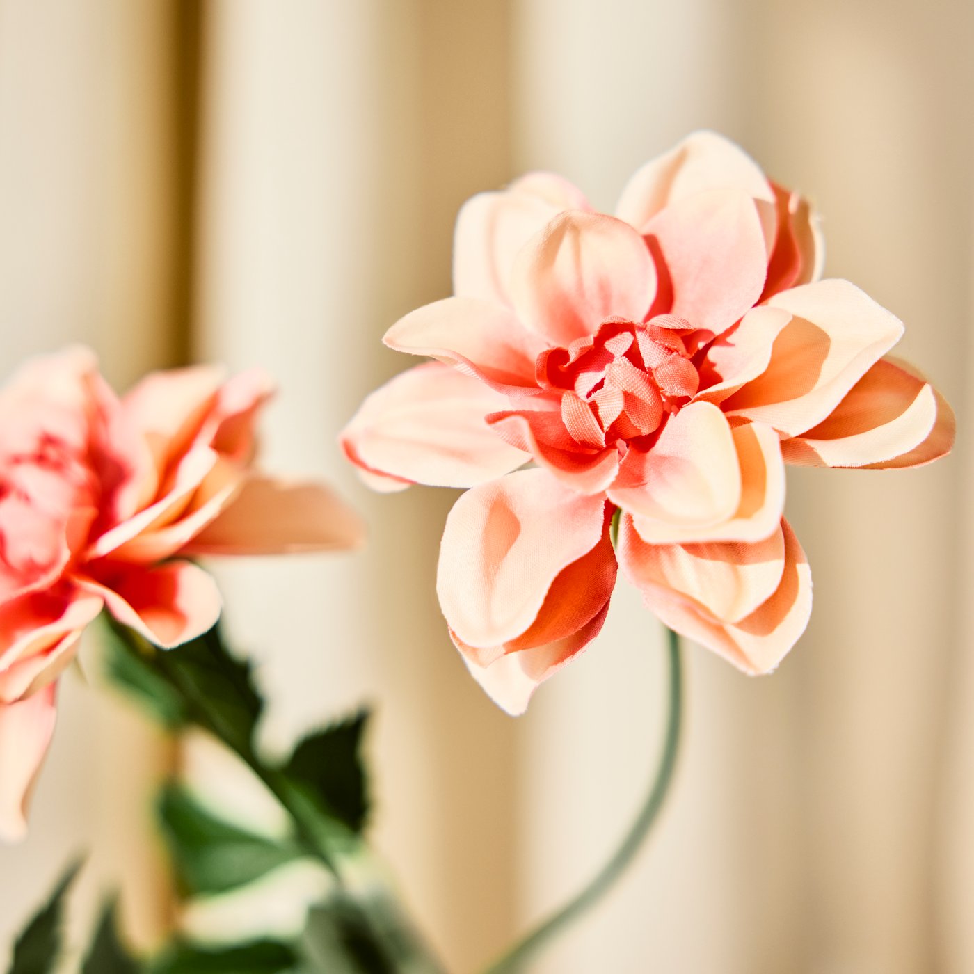 Nahaufnahme einer künstlichen rosa Dahlie mit mehreren Blütenblättern und grünen Blättern, aus der SMYCKA-Serie, vor neutralem Hintergrund.