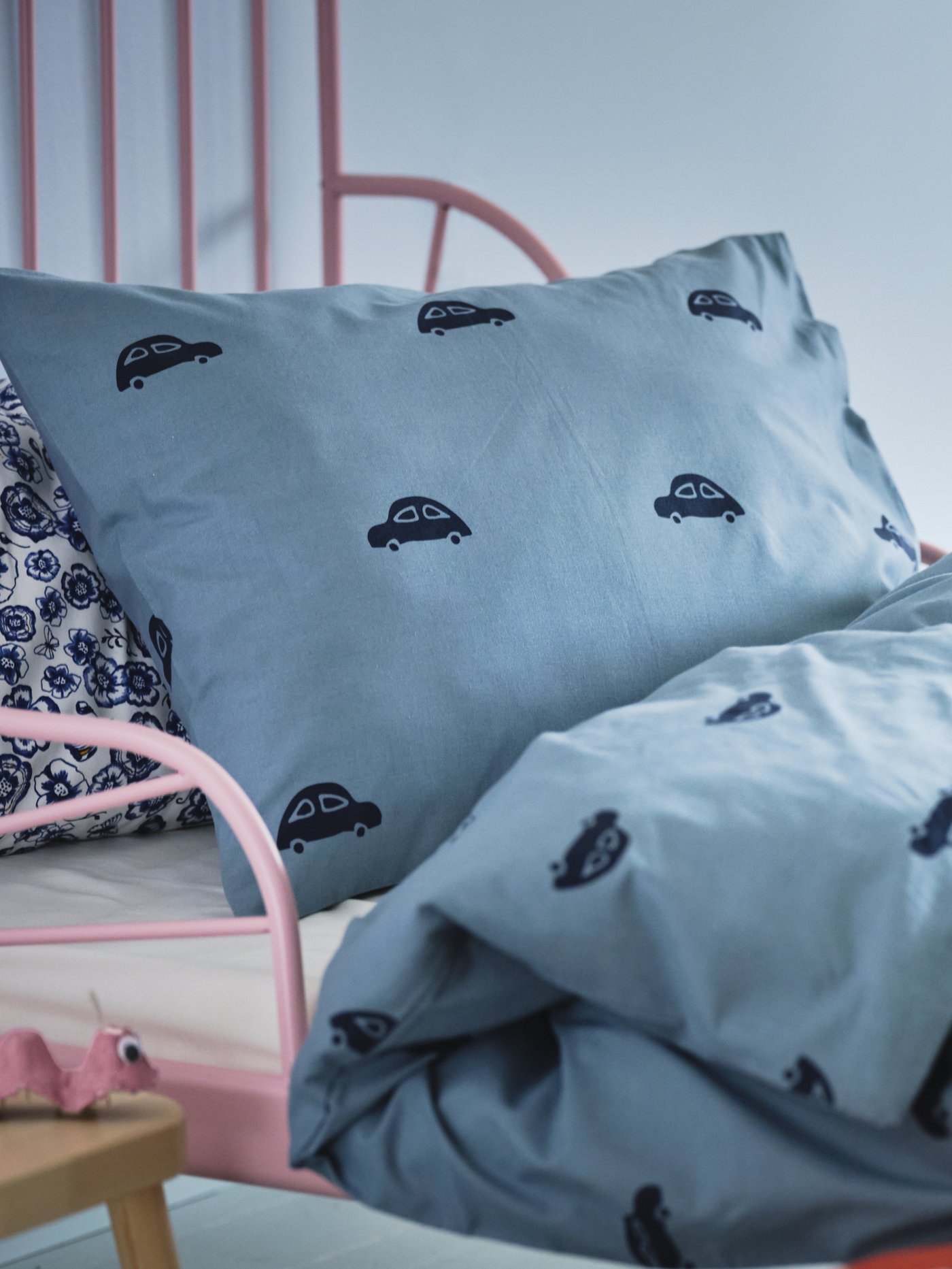 Dormitorio infantil con una cama, una almohada y un edredón con una funda de almohada y una funda nórdica con un estampado de coches.
