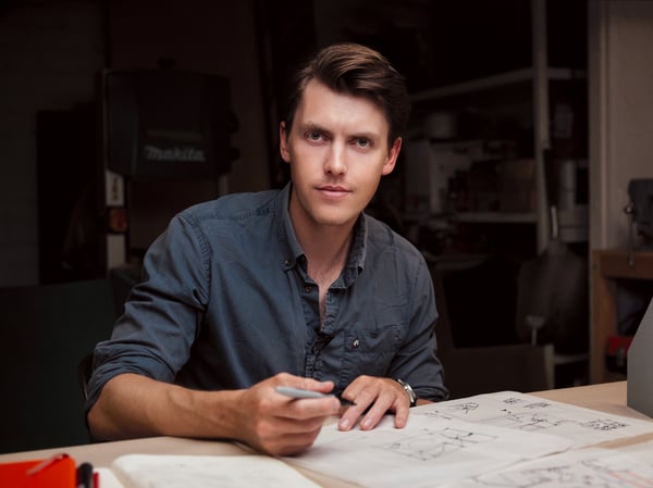 A man sitting behind a desk with a pen in his hand. He is looking into the camera.