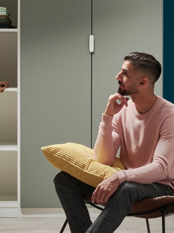 Un homem assis devant un meuble dressing vert avec un coussin sur les genoux.