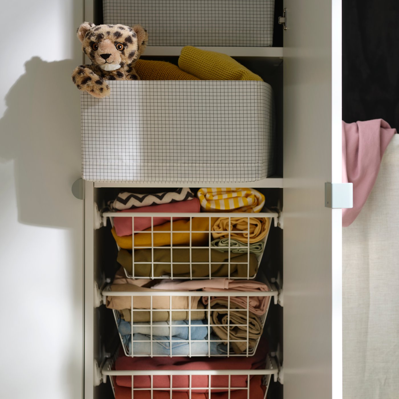 STUK storage case in a wardrobe, filled with folded clothes and a soft toy on top, beside hanging garments.