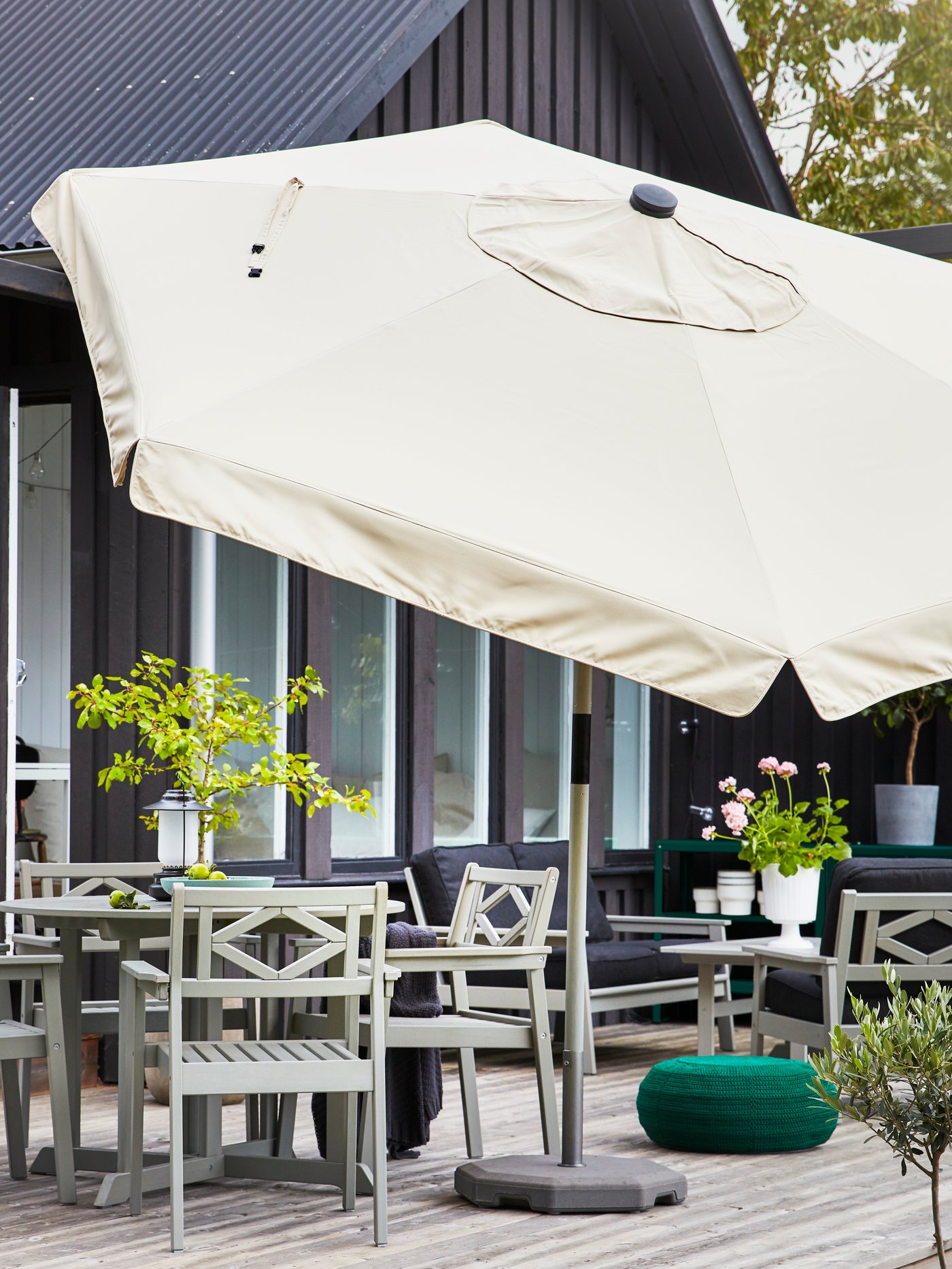 A big, beige parasol is standing next to an outdoor dining area that consists of a grey table and four grey chairs.