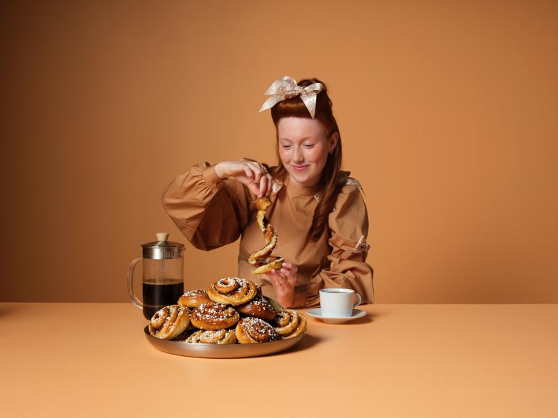 Eine junge Frau, die an einem Tisch sitzt und Zimtschnecken isst und eine Tasse Kaffe trinkt.