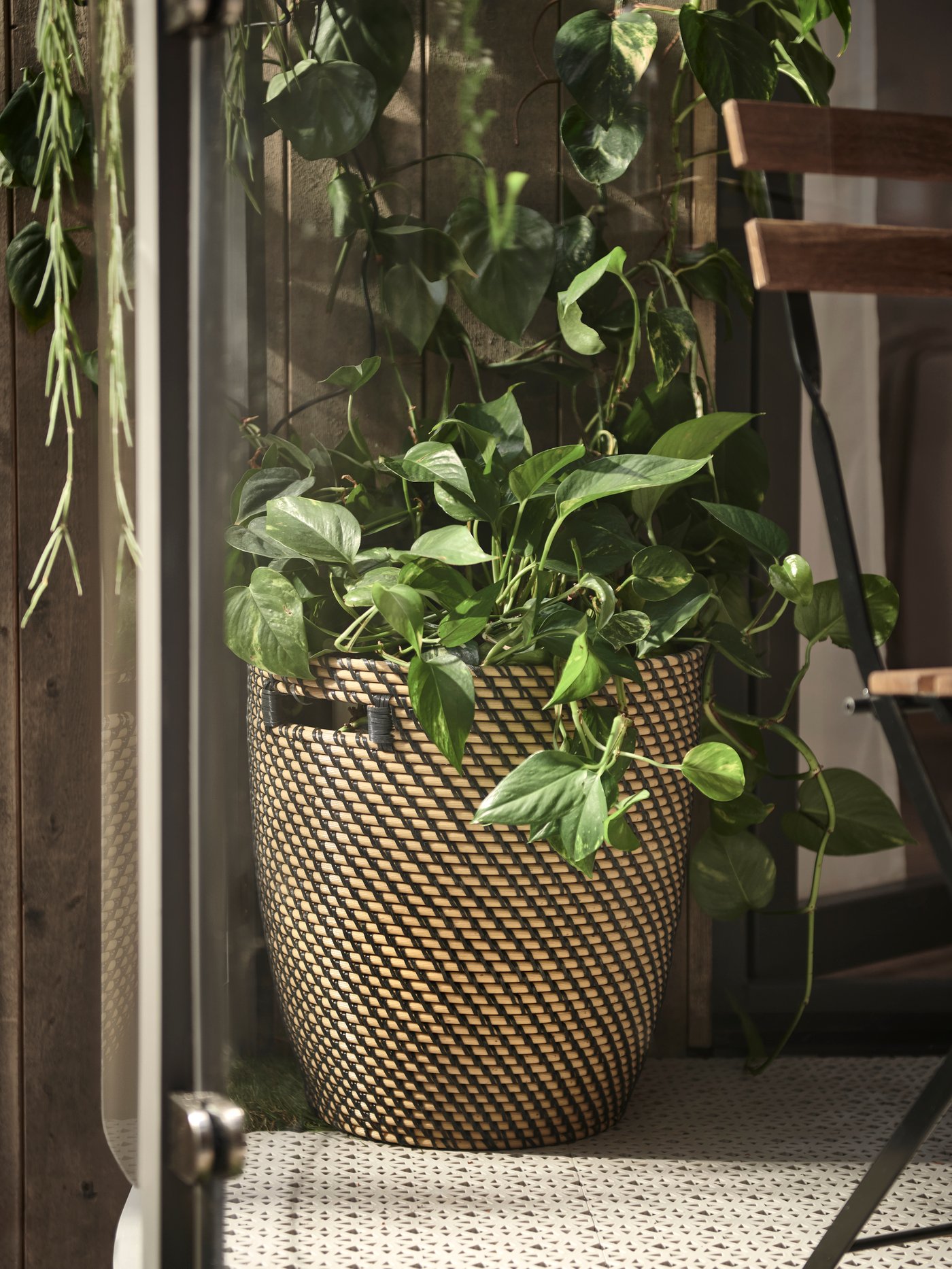 Exterior con una maceta RÅGKORN beige colocada sobre la tarima ALTAPPEN gris para exterior junto a la silla TÄRNÖ.