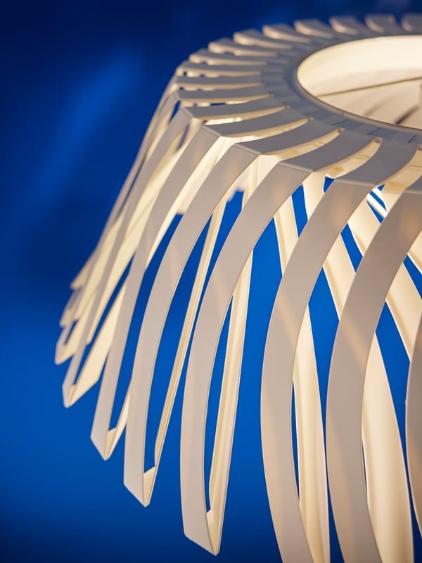 The detailing of the white shade of a lit YTLÄGE pendant lamp against an electric blue backdrop.