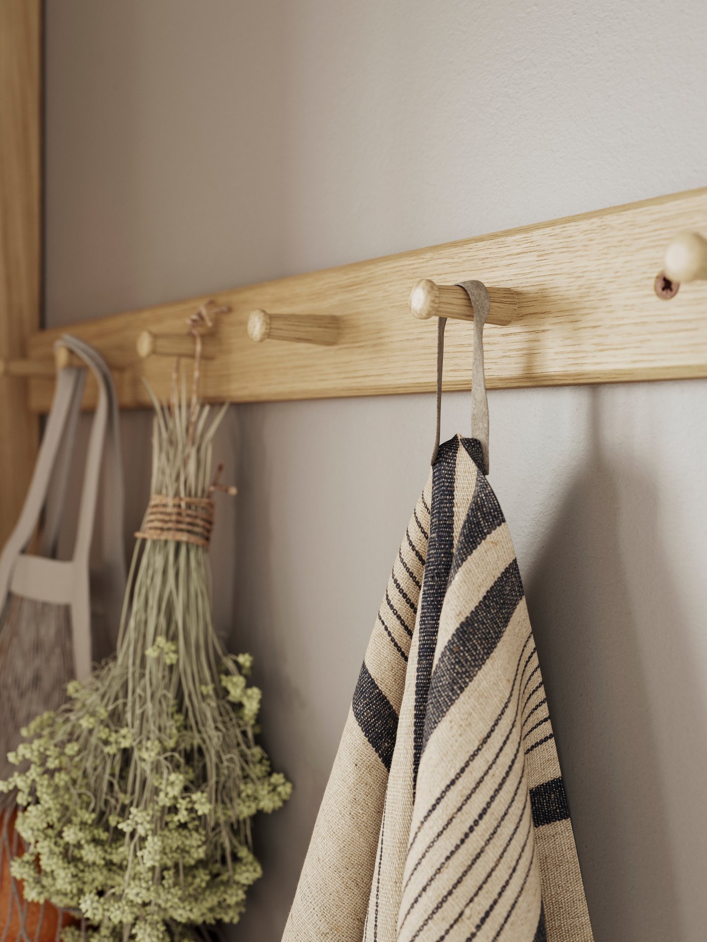 Trälist med runda knoppar på en vägg, där en randig handduk och en bunt torkade blommor hänger tillsammans med en tygpåse.
