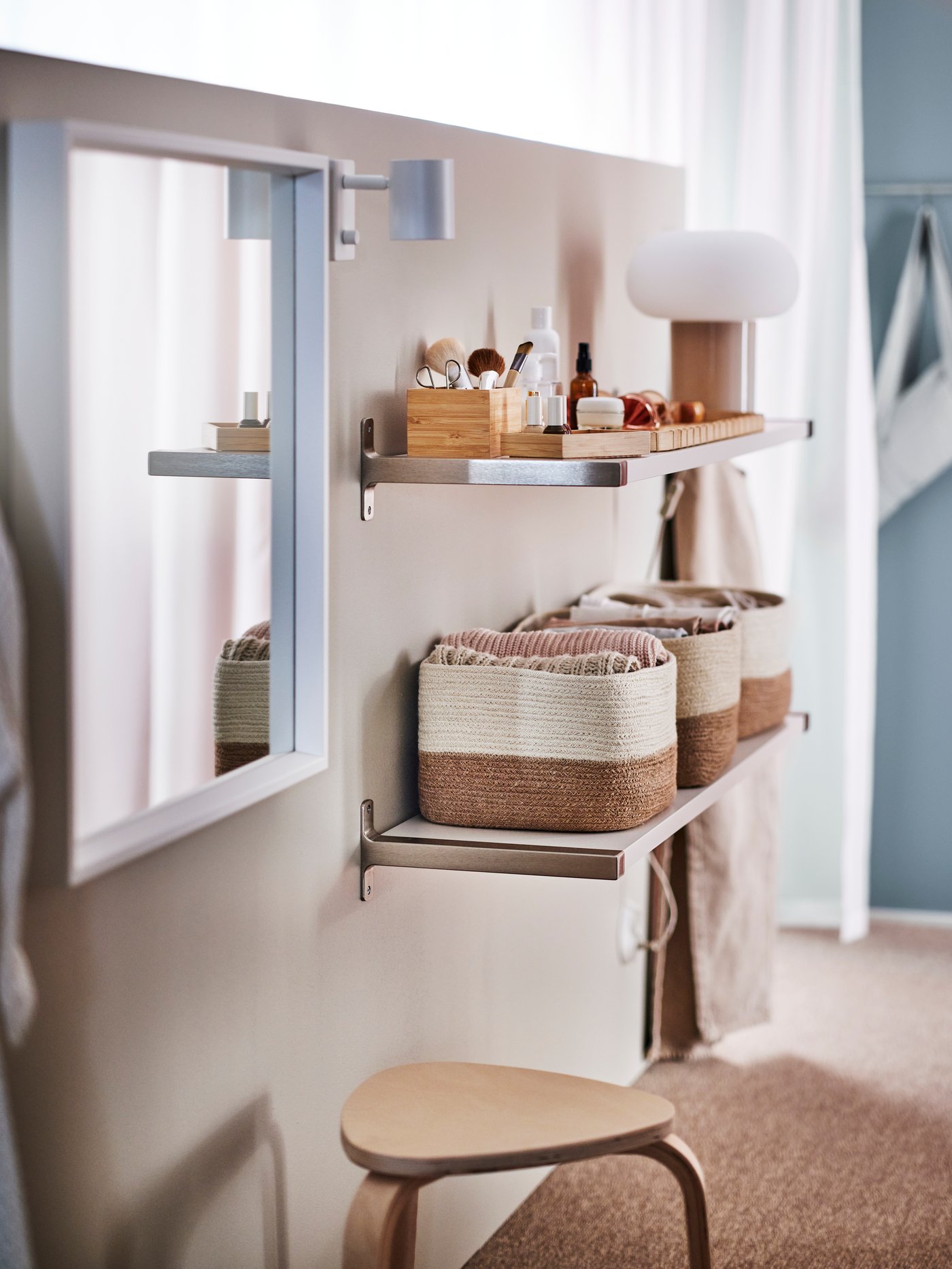 Two shelves on a wall with a white NISSEDAL mirror and a KYRRE stool by them. The lower shelf holds three LJUNGAN baskets.