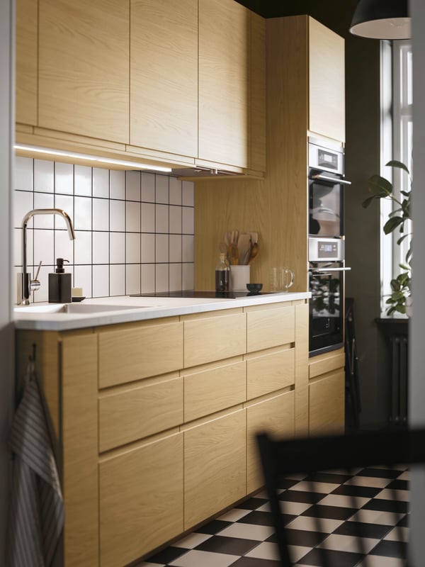 In una piccola cucina dal design lineare, diversi mobili base e pensili con frontali VOXTORP effetto rovere con maniglie integrate.