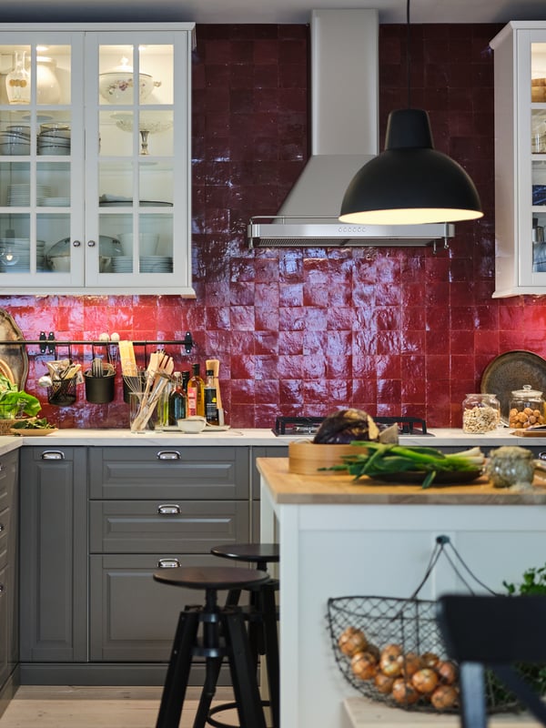 A red-tiled kitchen with grey base cabinets, white wall cabinets, white worktop, and a white island with a wooden worktop.