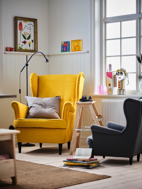 Living room featuring a yellow wing chair with extra neck support placed next to a grey children's armchair and a stepladder.