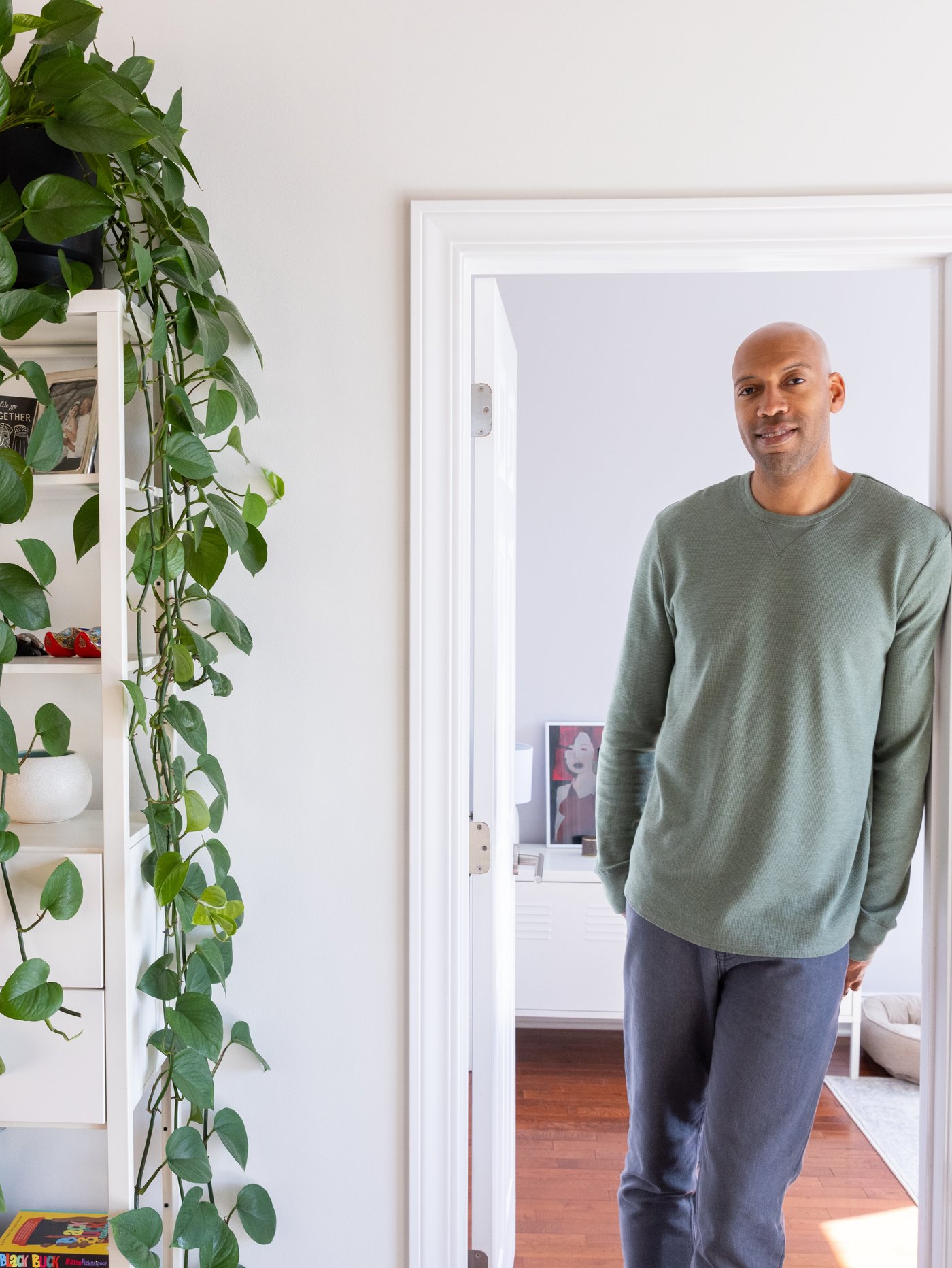 Man standing in clean white doorway, next to a bookcase with a plant hanging down.