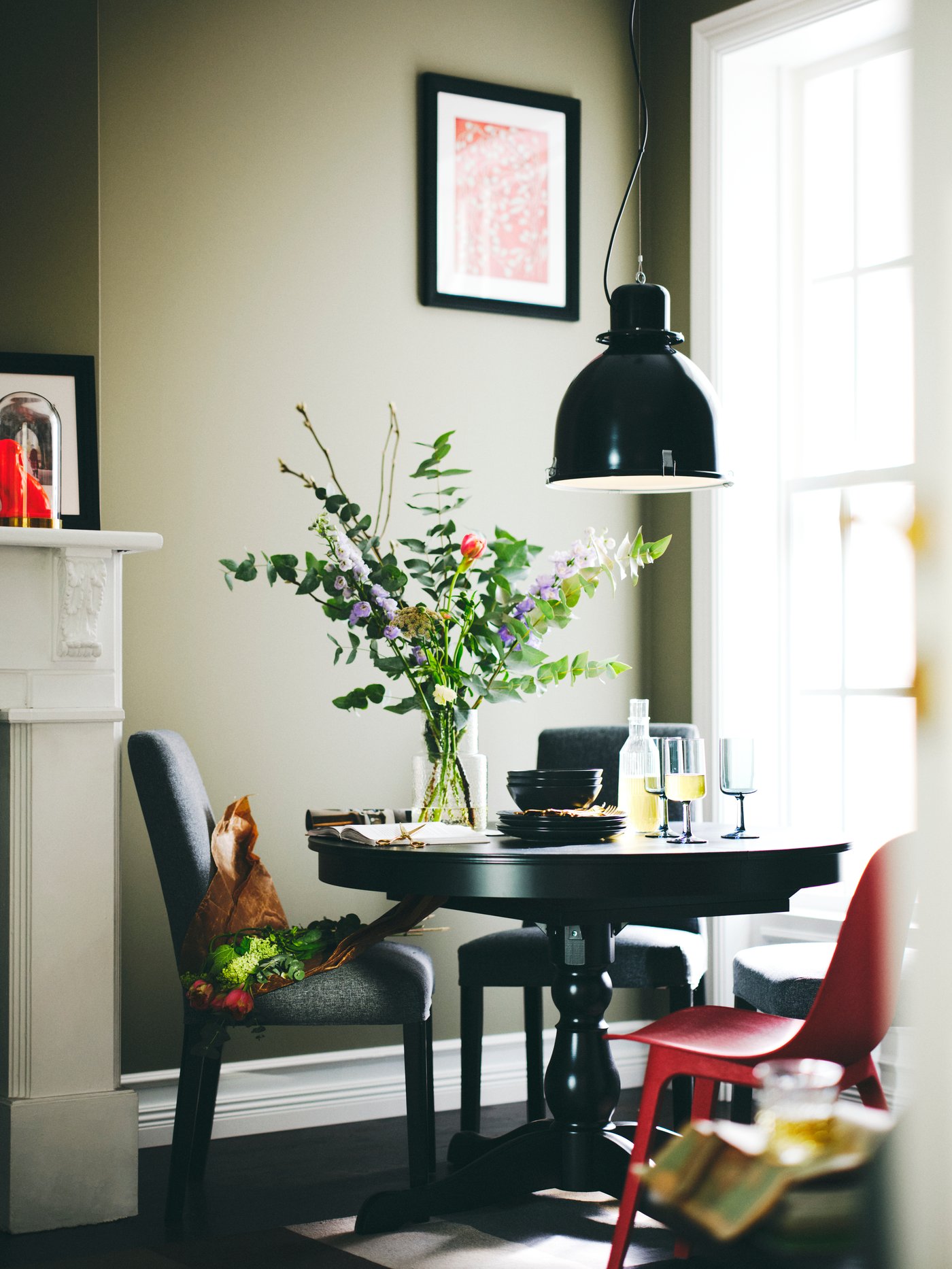 Dining room with a round extendable table made of wood, surrounded by 2 black chairs and a red chair. 