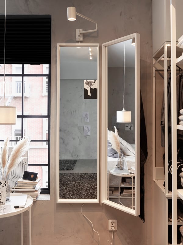 Bedroom with a wall lamp hanging above two mounted mirrors, with a tray table on the left and a bookcase on the right.