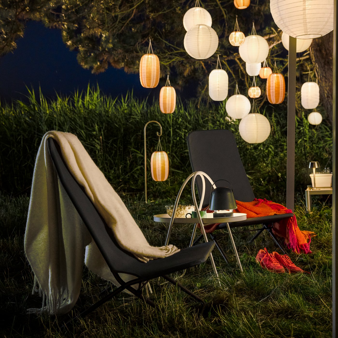 A cosy evening garden area with hanging lights features a dark grey VIGGSÖ lounge chair, surrounded by greenery.