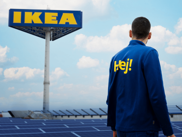 Zaměstnanec stojí před cedulí IKEA obklopenou solárními panely pod jasnou oblohou