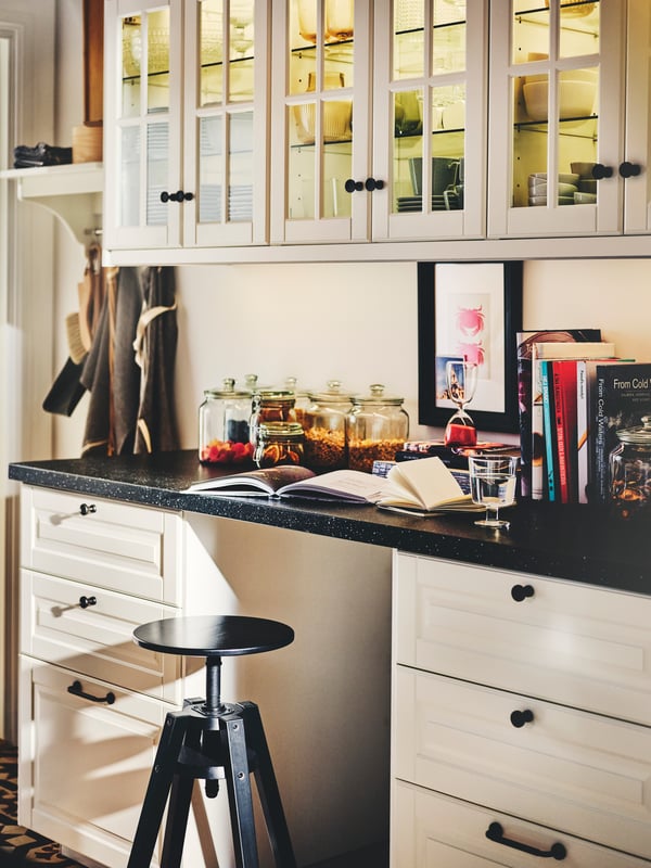 A kitchen with white BODBYN drawer fronts, SKRUVSHULT knobs, a black SÄLJAN worktop and a DALFRED bar stool.