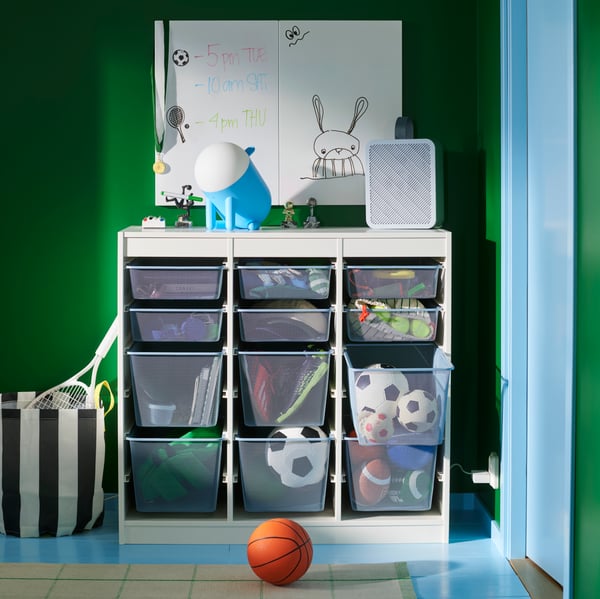 A TROFAST combination with mesh storage boxes storing sports balls and equipment, against a green wall in a children’s room.