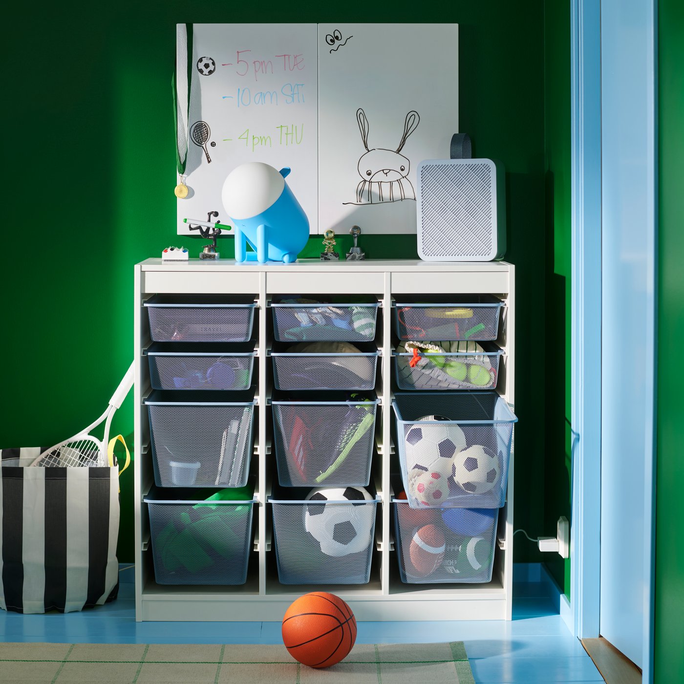 Uma combinação TROFAST com caixas de arrumação em rede para guardar bolas e equipamento desportivo, junto a uma parede verde num quarto de criança.