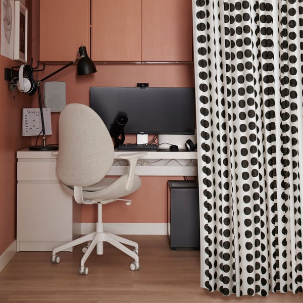 A half-open KLARASTINA curtain revealing a MALM desk and a HATTEFJÄLL swivel chair in an alcove used as a home office.