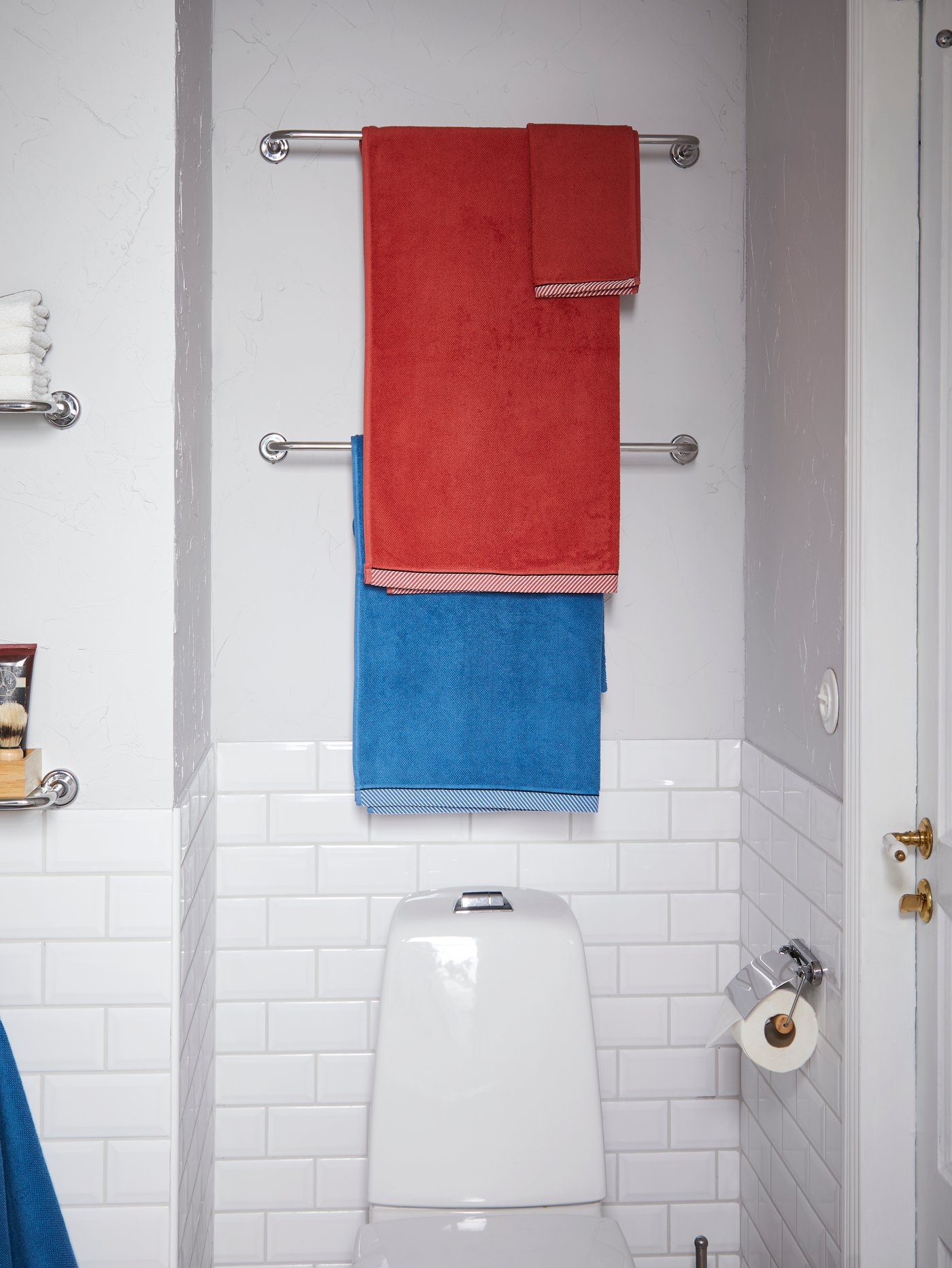 Dua selusur tuala VOXNAN dalam kesan krom diletakkan pada dinding sebelah atas tandas dan tuala bilik mandi digantung padanya.