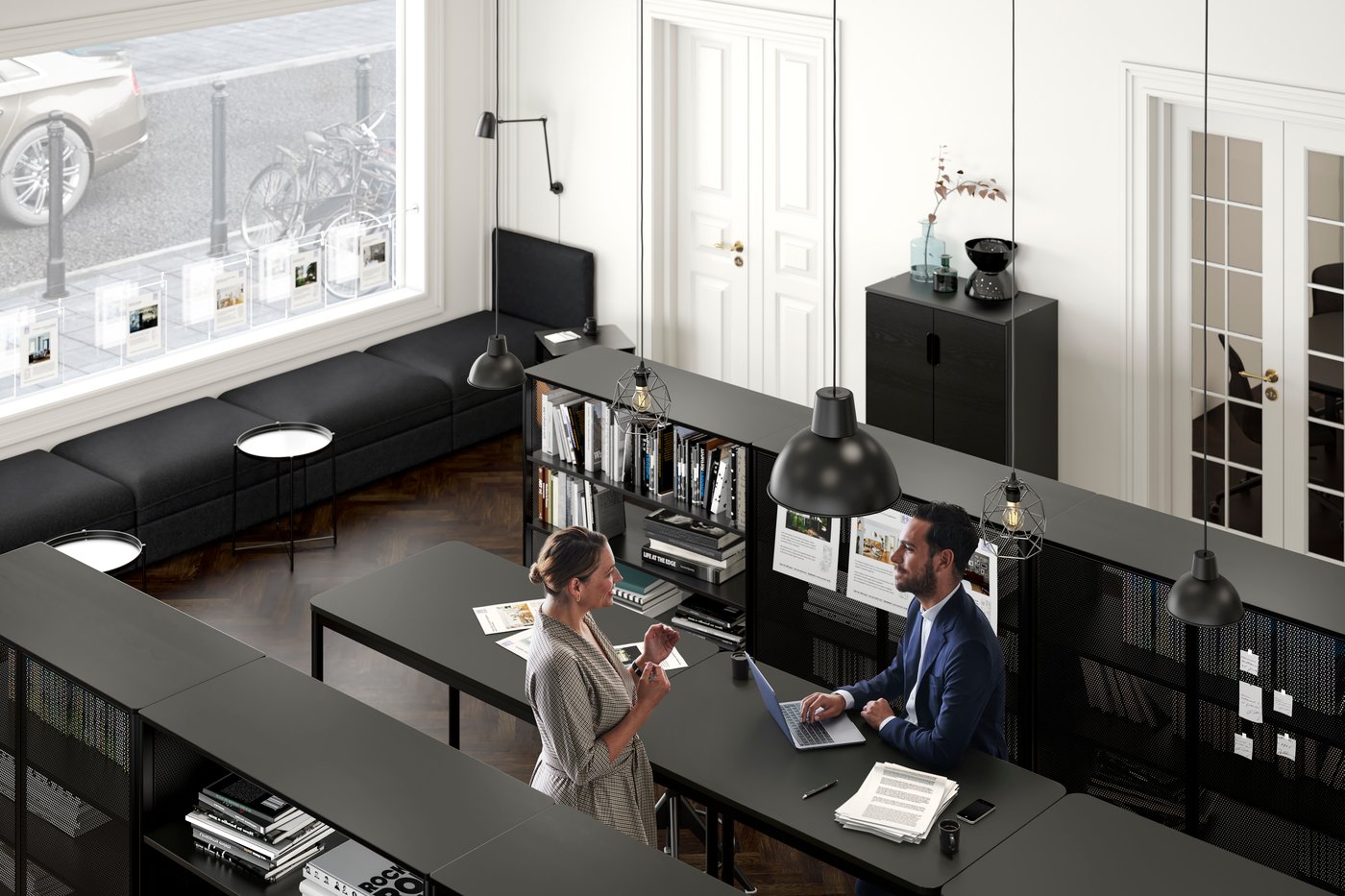 An office setting where a woman talks to a man in a suit who sits with his laptop by a TOMMARYD table.