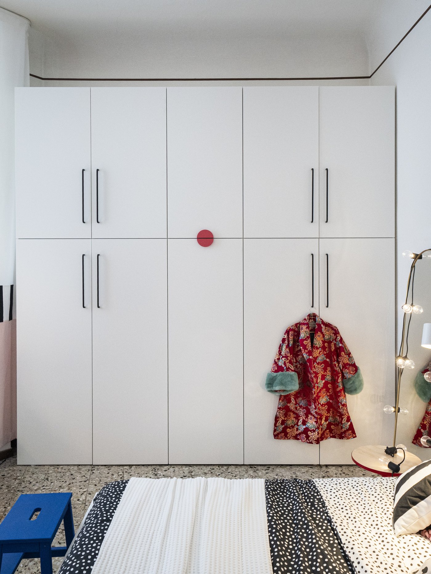 Grande guardaroba PLATSA bianco a tutta parete con lunghe maniglie nere, in camera da letto, con vestaglia rossa appesa a un’anta.