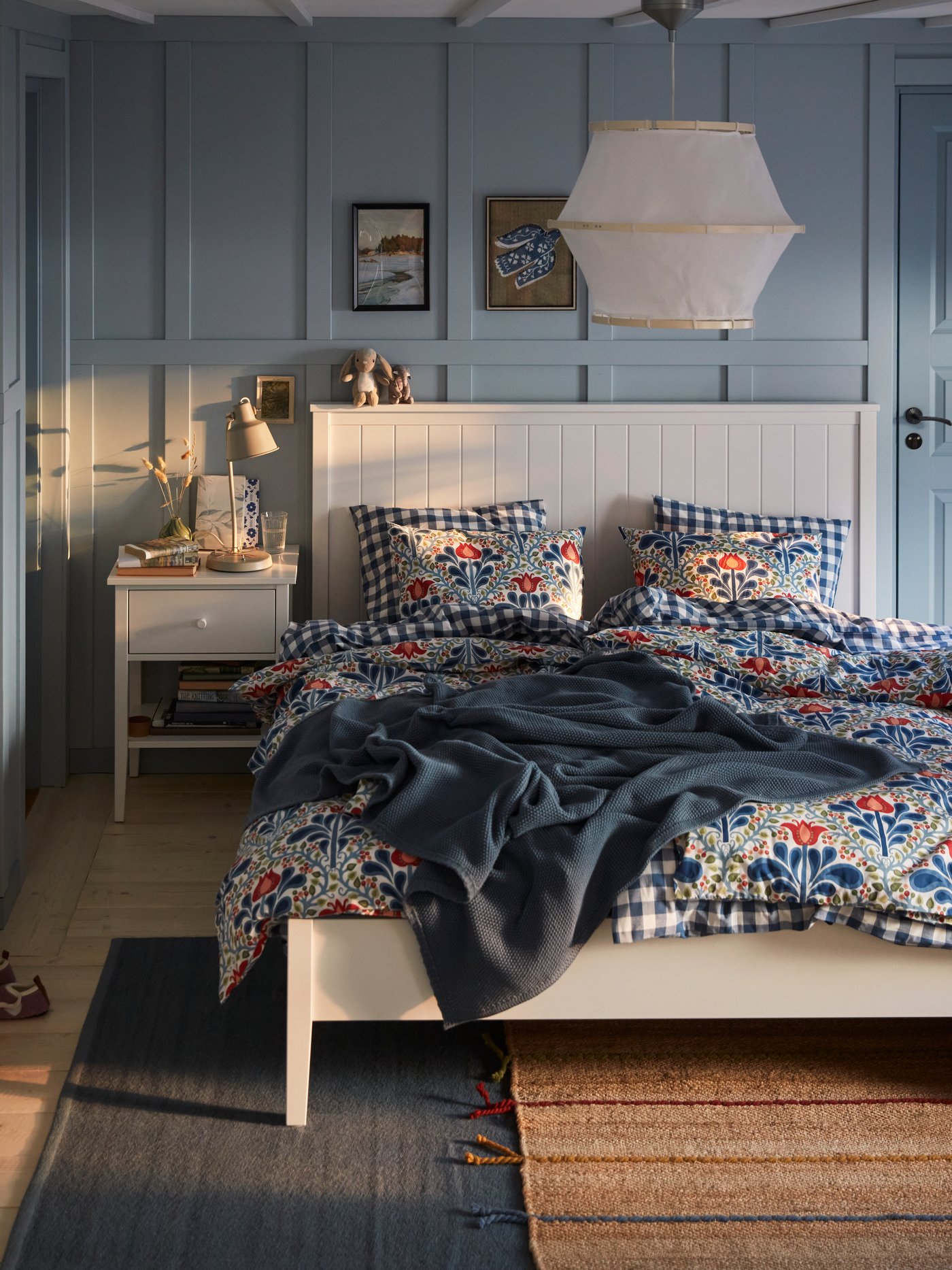 A blue bedroom with a white GULLABERG bed with floral bed linen, a blue throw and a white bedside table.