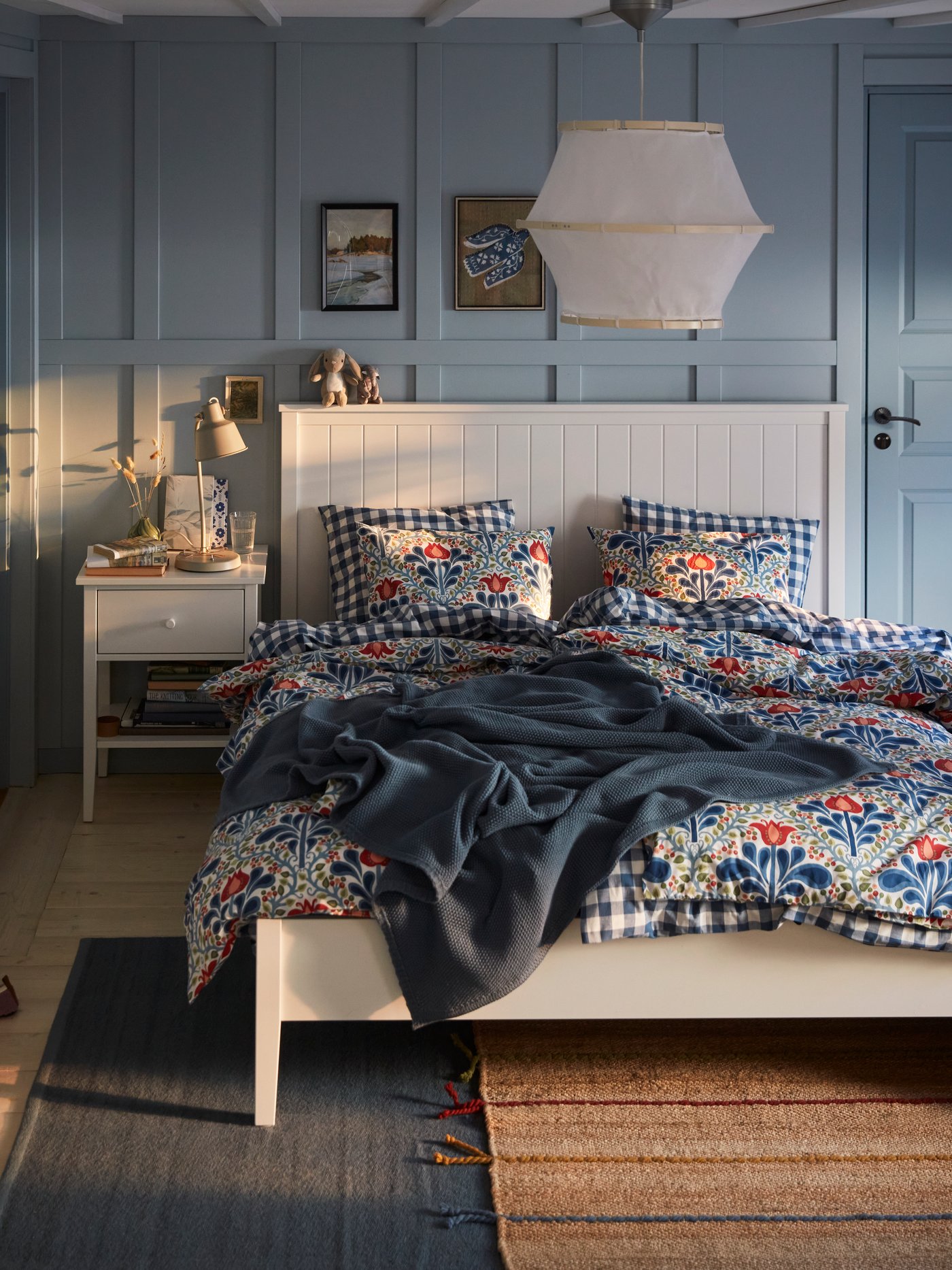 A blue bedroom with a white GULLABERG bed with floral bed linen, a blue throw and a white bedside table.