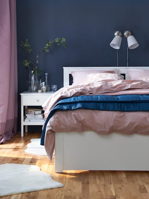 Cadre de lit SONGESAND blanc dans une pièce avec plancher en bois et tapis blancs. Le lit est fait avec du linge de lit bleu et rose.